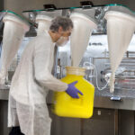 SAFECAN : une solution innovante pour la gestion des déchets en environnements contrôlés 8 Opérateur manipulant un conteneur avec le système SafeCan devant un isolateur pharmaceutique en zone confinée