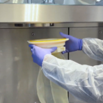 Simplifiez la gestion de vos déchets en environnements stériles 4 Opérateur manipulant un sac souple de transfert sous isolateur pharmaceutique dans un environnement de confinement