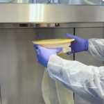 Simplifiez la gestion de vos déchets en environnements stériles 4 Opérateur manipulant un sac souple de transfert sous isolateur pharmaceutique dans un environnement de confinement